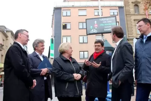 „GO Karlsruhe“-Projektleiter Professor Christoph Hupfer (Mitte, roter Schal) vor einem Display, das Radlern Ausweichrouten anzei