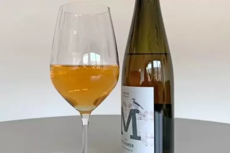 Auf einem Tisch steht ein Glas mit Orange-Wein, eingeschenkt von einer Flasche mit einem Orange-Wein der Rebsorte Silvaner.