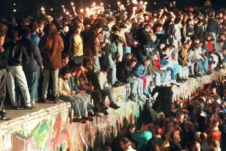 Jubelnde Menschen sitzen mit Wunderkerzen auf der Berliner Mauer.