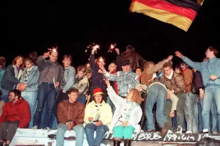Menschen auf der Berliner Mauer freuen sich über die Öffnung der deutsch-deutschen Grenzen.