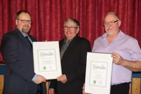 Ortsbürgermeister Marcel Form (links) händigt nach der Laudatio die Urkunden zur Ehrenbürgerschaft an Helmut Burgdöfer (Mitte) u