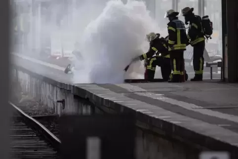 Einsatzkräfte der Feuerwehr stehen während eines Löscheinsatzes auf einem Gleis des Hauptbahnhofs. 